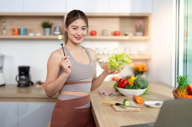 Bir kadın elinde bir kase salata tutarken gülümsüyor, sağlıklı beslenme alışkanlıklarını temsil ediyor..
