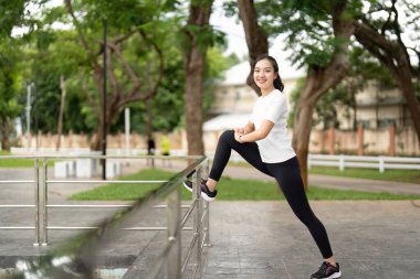 Parktaki korkuluklara bacağını uzatan bir kadın kendine güven ve zindelik sergiliyor. Etkin yaşam tarzı ve açık hava refahını vurgular.