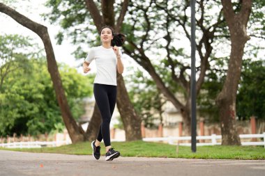 Genç bir kadın parkta neşeyle koşuyor, aktif bir yaşam tarzını ve dışarıda sağlık için yapılan egzersizin faydalarını temsil ediyor..