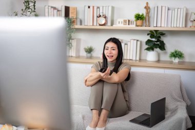 Neşeli bir kadın elinde uzaktan kumandayla kanepeye oturur ve sıcak bir oturma odasında en sevdiği şovun tadını çıkarır..