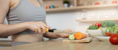 Genç bir kadın havuç ve salatalıkları ustalıkla doğruyor. Mutfaktaki sağlığını ve sağlıklı yemek yapma alışkanlıklarını ön plana çıkarıyor..