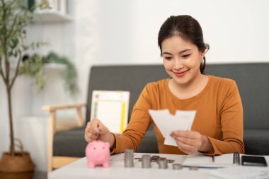 Genç bir kadın birikimlerini bir domuz kumbarasına yatırırken, bütçe ve mali farkındalığı vurguluyor..