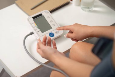 Bir kadın dijital tansiyon monitörünü işaret ederek, sağlık ve kişisel sağlığa odaklanıyor.