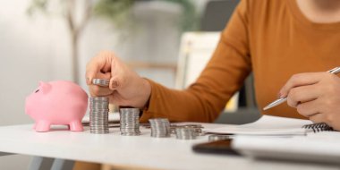 Bir kadın, parasal planlama ve tasarrufların önemini vurgulayarak sikkelerini pembe bir kumbaranın yanında düzenliyor..