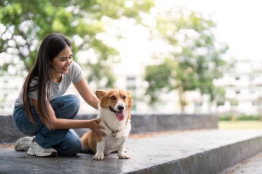 Genç bir kadın, Corgisiyle bir anlık bir bağ kurmaktan zevk alır, onu sevgiyle açık havada okşar..