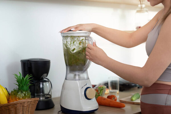 A young woman blends fresh vegetables and greens in a blender, focusing on healthy meal preparation in her kitchen.