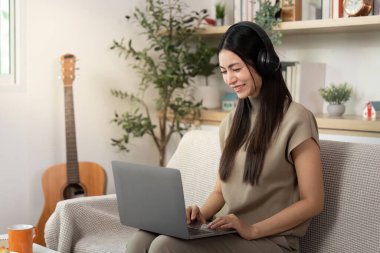 Genç bir kadın bilgisayarını kulaklıkla kullanırken gülümsüyor, uzaktan kumandalı bir işte çalışıyor ya da evde internetten öğreniyor..