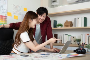 UX ve UI tasarımlarını birlikte inceleyen iki genç profesyonel parlak, modern bir ofiste dizüstü bilgisayarın ekranına işaret ediyor..