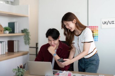 Modern bir ofiste iki profesyonelin UX UI kavramlarını bilgisayar ve akıllı telefon kullanarak analiz ettiği odaklanmış bir tasarım oturumu..