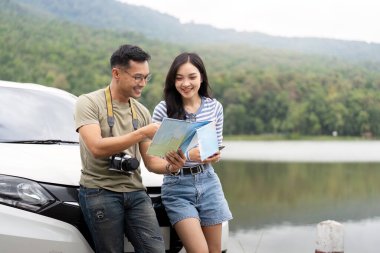 Genç bir çift arabalarının yanında durup haritaya bakarken mutlu bir şekilde seyahat planlarını tartışıyor ve açık havanın tadını çıkarıyor..
