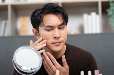 Cildini yakından inceleyen genç bir adam cilt bakımını ve özbakımını vurgulayarak cilt bakımını uyguluyor..