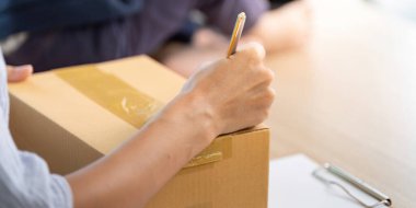 Bir el, internet üzerinden satış sürecinin detaylarını vurgulayarak, bir nakliye kutusunun üzerine yazıyor..
