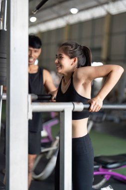 Bir bayan atlet barfiks çekerken antrenörü cesaret ve destek veriyor, fitness özverisini vurguluyor..