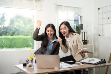 İki iş ortağı bir dizüstü bilgisayarın önünde sevinçle kutlama yapıyor, heyecan ve takım çalışması ifade ediyorlar..