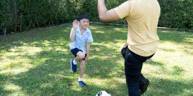 Genç bir çocuk, anne babasıyla futbol oynuyor. Arka bahçede oyuncu etkileşimi ve beceri geliştirmesi sergiliyor..
