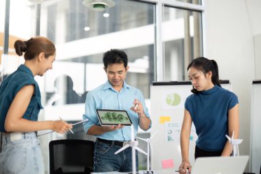 Çeşitli bir ekip yenilenebilir enerji stratejilerini modern bir çalışma alanında sürdürülebilirlik ve ESG 'yi vurgulayarak bir tablette sergiliyor..