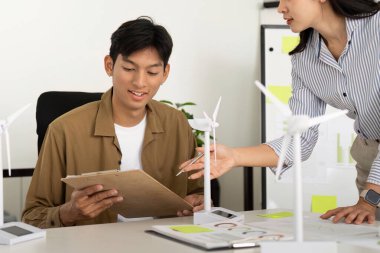 Genç bir profesyonel, yenilenebilir enerji planlarını incelerken modern bir ofiste rüzgar türbini modelleri hakkında bir tartışmaya girişiyor..