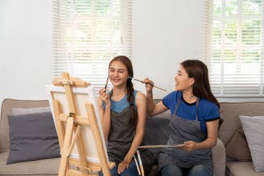 İki genç kadın, tuvale resim yaparken, yaratıcılıklarını sergilerken ve rahat bir oturma odasında bağ kurarken keyifli bir anı paylaşıyorlar..