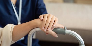 Bir bakıcı, yaşlı bir kadına destek olur, elini bir yürütece koyar, günlük aktivitelerde bağımsızlık ve güvenliği teşvik eder..