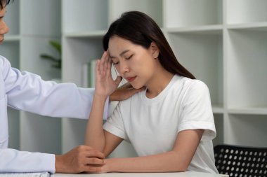 Bir sağlık uzmanı, tıbbi danışma sırasında baş ağrısı çeken bir kadını rahatlatır ve hasta bakımı ve empatiyi vurgular.