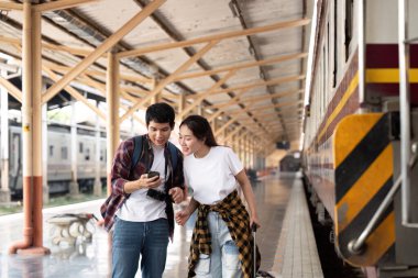 Genç bir çift, tren istasyonundaki akıllı telefondan seyahat planlarını kontrol ederken heyecanlarını paylaşıyor..
