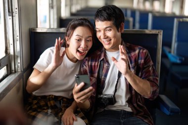 Bir çift trende video izlemekten zevk alıyor. Seyahat deneyimleri sırasında kahkaha ve neşe paylaşıyorlar..