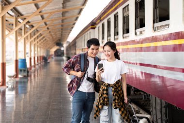 Tren istasyonunda neşeli bir anı paylaşan genç bir çift akıllı telefonlarına bakıp seyahat anılarını yakalıyor..