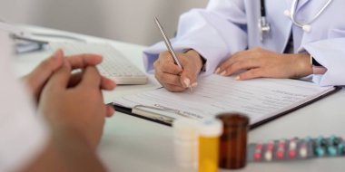 Bir sağlık hizmetleri uzmanı, klinik ortamdaki bir muayene sırasında hastanın tıbbi bilgilerini kaydeder..