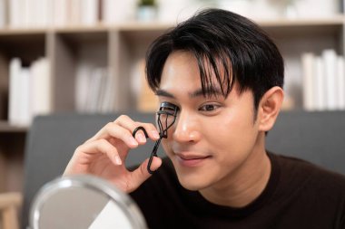 Genç bir adam bir kirpik bigudisi kullanır, titiz bir bakım rutinini vurgulayarak görünüşünü geliştirmeye odaklanır..