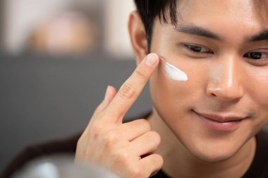 Genç bir adamın yanağına krem sürerken, cilt bakımını ve özel bakımını gösterirken çekilmiş yakın plan bir fotoğrafı..