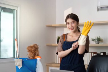 Sarı eldivenler giyerken gülümseyen bir insan, çeşitli aletlerle temizlik yapmaya hazır, evde bakım için proaktif bir yaklaşım sergiliyor..