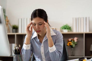 Genç bir kadın bilgisayarının başında çalışırken şakaklarını gıcık ediyor. Ofis sendromunun ruh sağlığı üzerindeki etkisini vurguluyor..
