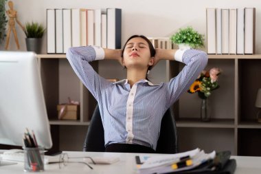 Stresli bir iş gününden sonra masasında dinlenmek için sandalyesine yaslanan genç bir kadın ofis sendromunu yansıtıyor..