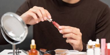 Genç bir adam, makyaj rutinindeki detaylara dikkat çekmek için tüpten dudak parlatıcısı sürüyor..