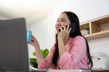 Evde çalışırken telefonla konuşan genç bir kadın, görevleri neşeli bir tavırla dengeliyor..