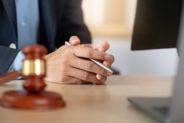 Bir avukat, elinde kalem tutarak ve düşünceli bir tavır sergileyerek müvekkilleriyle yasal bir ortamda görüşmeye hazır bir şekilde konsültasyona hazırlanır..