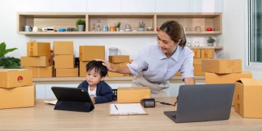 Bir anne, iş ve aile hayatının dengesini gözler önüne seren paketlerle dolu bir evde çocuğunu tabletle destekliyor..