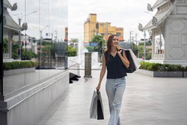 Genç bir kadın Kara Cuma 'da alışveriş çantasıyla mutlu bir şekilde yürüyor, hareketli şehir atmosferinin tadını çıkarıyor..