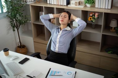 Masasında oturan genç bir profesyonel, görünür bir şekilde stresli, elleri başının üstünde, ofis sendromunun etkisini gösteriyor..