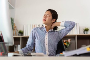 Genç bir profesyonel masasında çalışırken acı çekiyor, ofis sendromunun sağlık üzerindeki etkilerini vurguluyor..