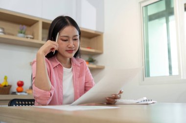 Evinde çalışan genç bir kadın masasında evrakları inceliyor, verimliliği ve konsantrasyonu somutlaştırıyor..