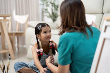 Genç bir kız, onlar oturma odasında yaratıcı bir resim seansının keyfini çıkarırken annesiyle dikkatlice konuşur..