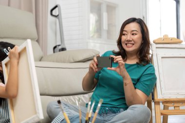 Bir anne, evinde sanatsal bir ifade ve sevgi sergileyerek yaratıcı bir resim yaparken kızının fotoğraflarını çeker..