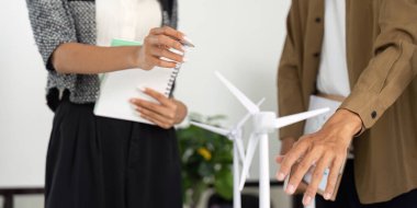 İki profesyonel, tartışmalarında sürdürülebilirlik ve yenilenebilir enerjiyi vurgulayan bir rüzgar türbini modelini inceliyor.