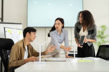 Bir ekip yenilenebilir enerji projeleri üzerinde işbirliği yapar, modelleri analiz eder ve modern bir ofiste sürdürülebilirlik stratejilerini tartışır..