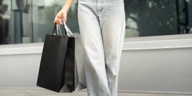 Genç bir kadın alışveriş torbalarıyla yürüyor, Kara Cuma satışları ve tüketici heyecanı ruhunu somutlaştırıyor..