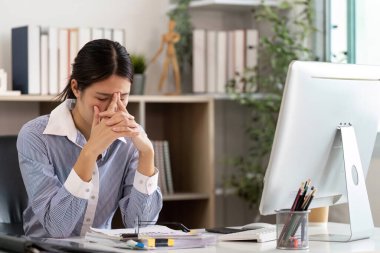 Masasındaki stresli bir kadın şakaklarını ovuyor. Modern bir çalışma alanında ofis sendromu ve duygusal yorgunluk belirtileri gösteriyor..