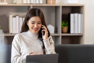 Genç bir kadın telefon görüşmesi sırasında gülümsüyor, şık bir ev ofisinde iş ve özel hayatını dengeliyor..