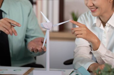 Modern bir ofiste rüzgar türbini modelini incelerken ESG stratejilerini tartışan iş adamları.