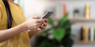 Genç bir kadın akıllı telefonuyla meşgul oluyor, teknolojinin günlük yaşamdaki entegrasyonunu şık bir ev ortamında sergiliyor..